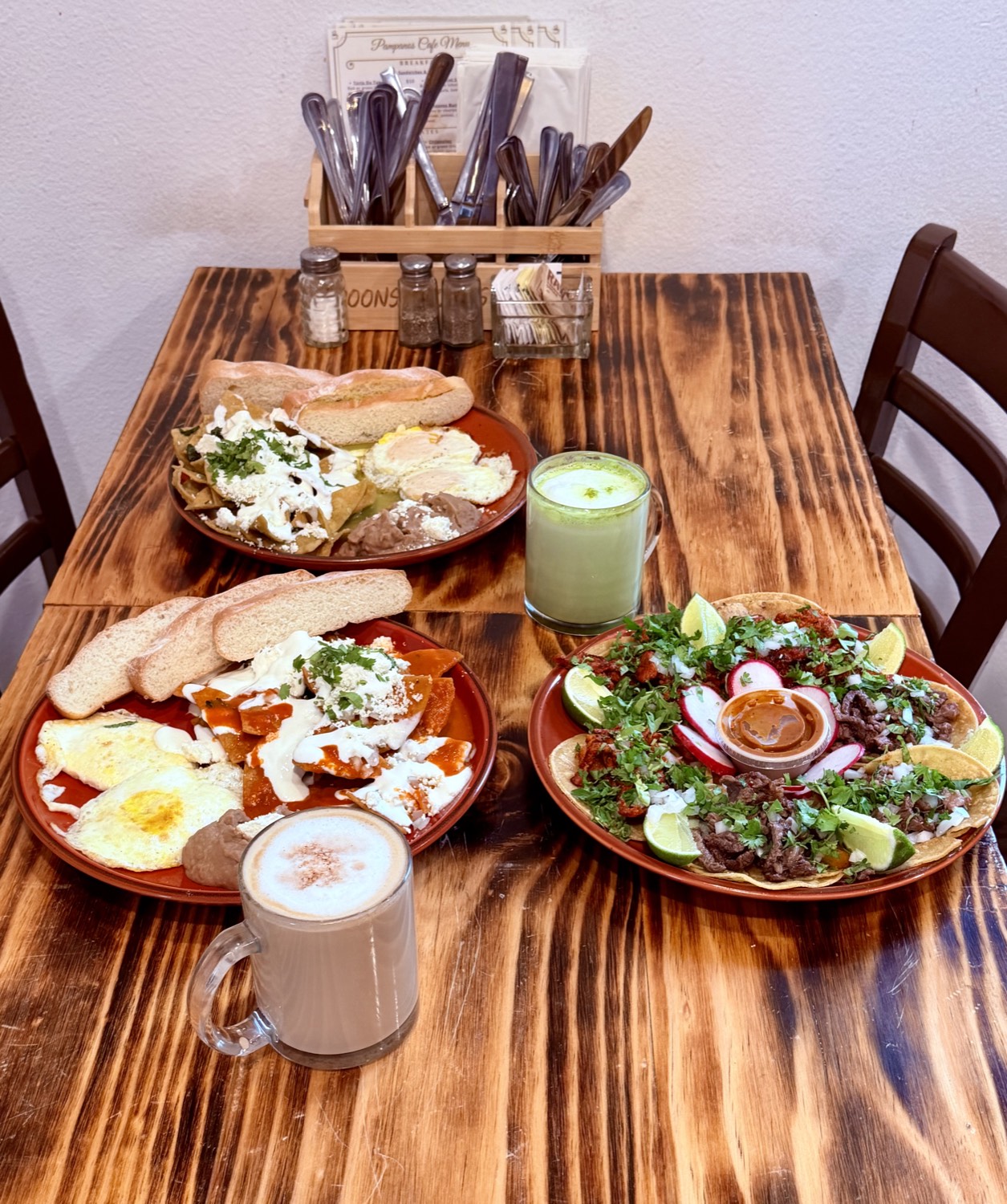 A table at Pampano's Cafe — two chilaquiles plates, a platter of asada and pastor tacos, a matcha latte and a horchata latte